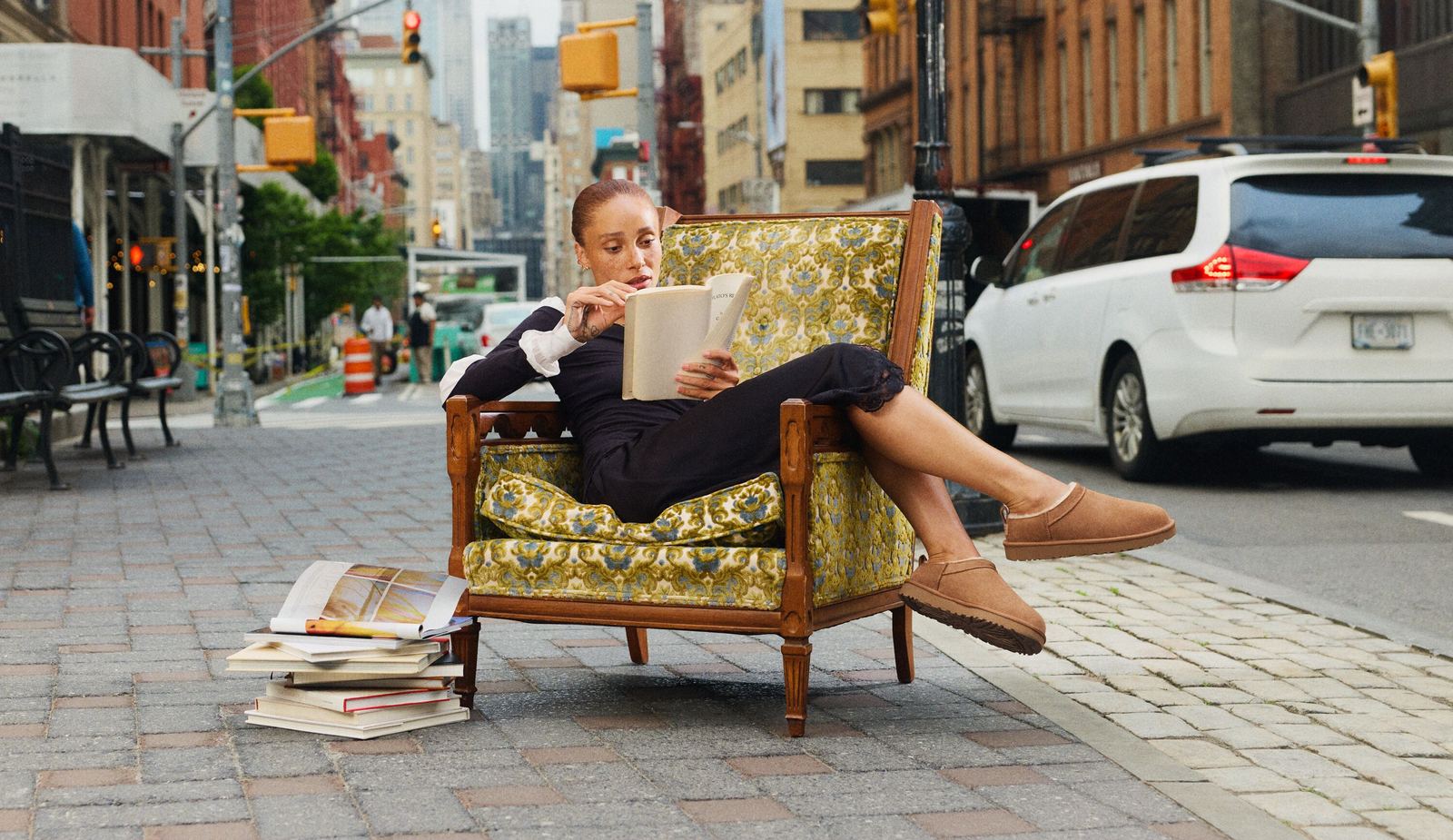 UGG’nin 2026 sonbahar kampanyası Born to Feel: New York kaldırımına konmuş desenli bir koltukta kitap okuyan bir kadın